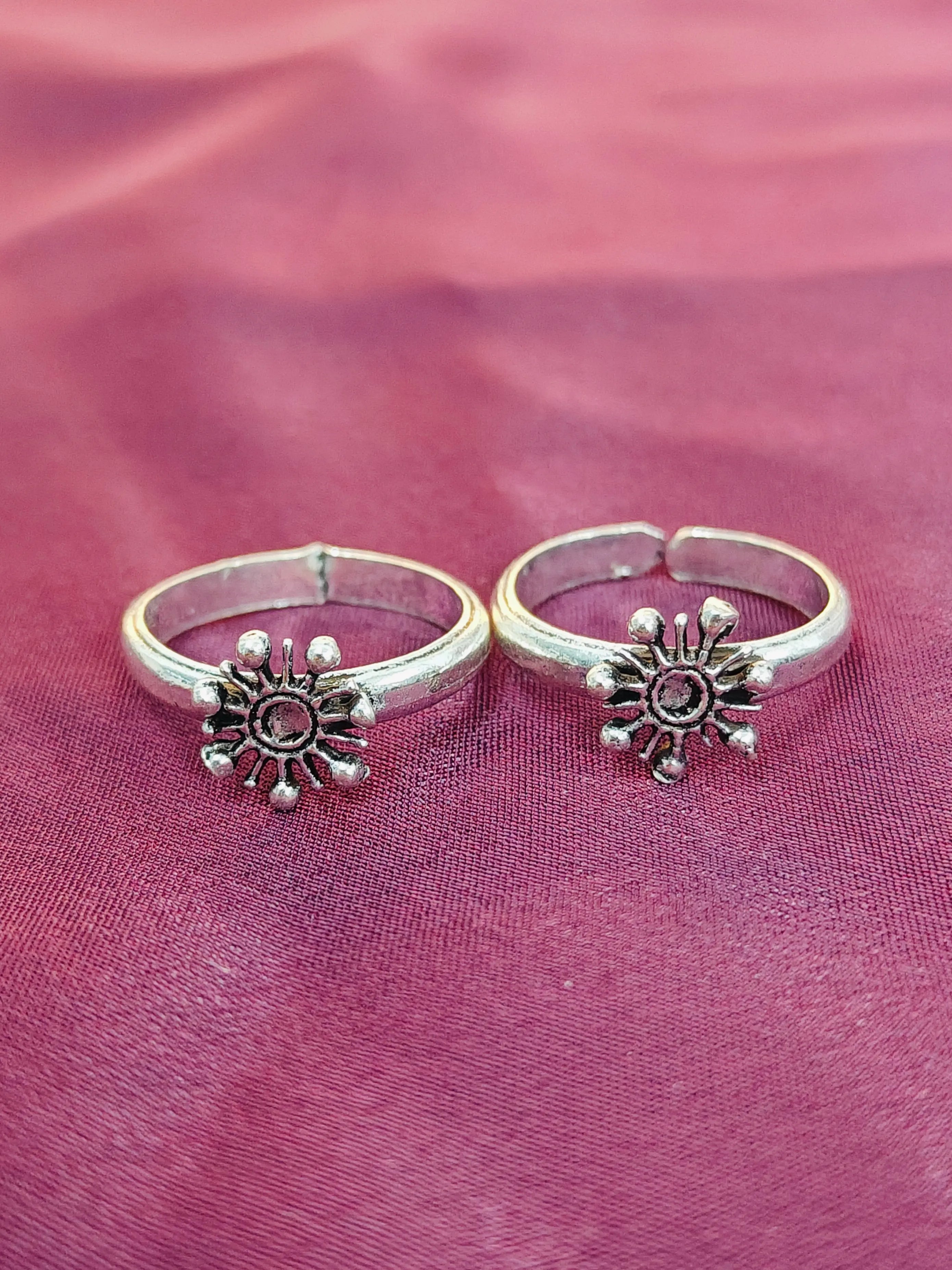 Two silver sun-shaped rings on a pink fabric background